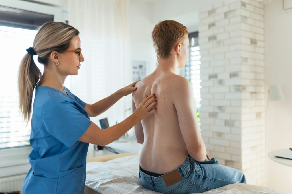 An orthopedist examines the spine, posture, and spinal deformities of teenage patient. Teenage boy