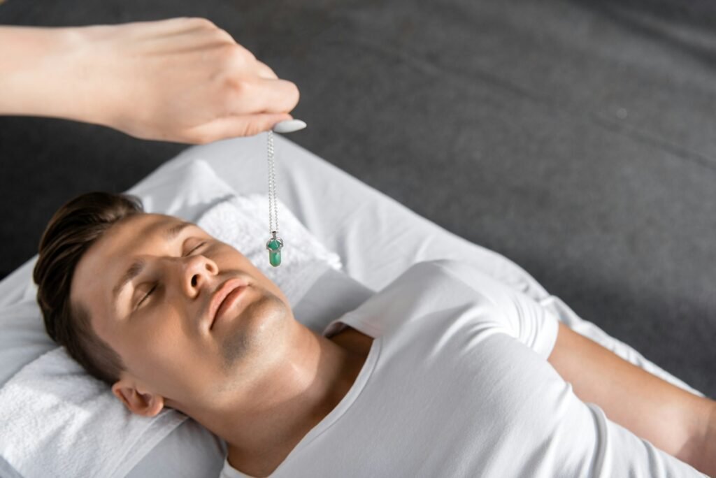 cropped view of hypnotist standing near man on massage table and holding green stone